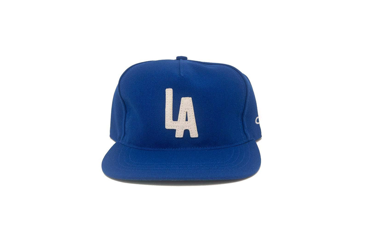 A royal blue flat-brim baseball cap featuring a white embroidered 'LA' logo on the front and a small white embroidered 'C' on the side, set against a plain white background.