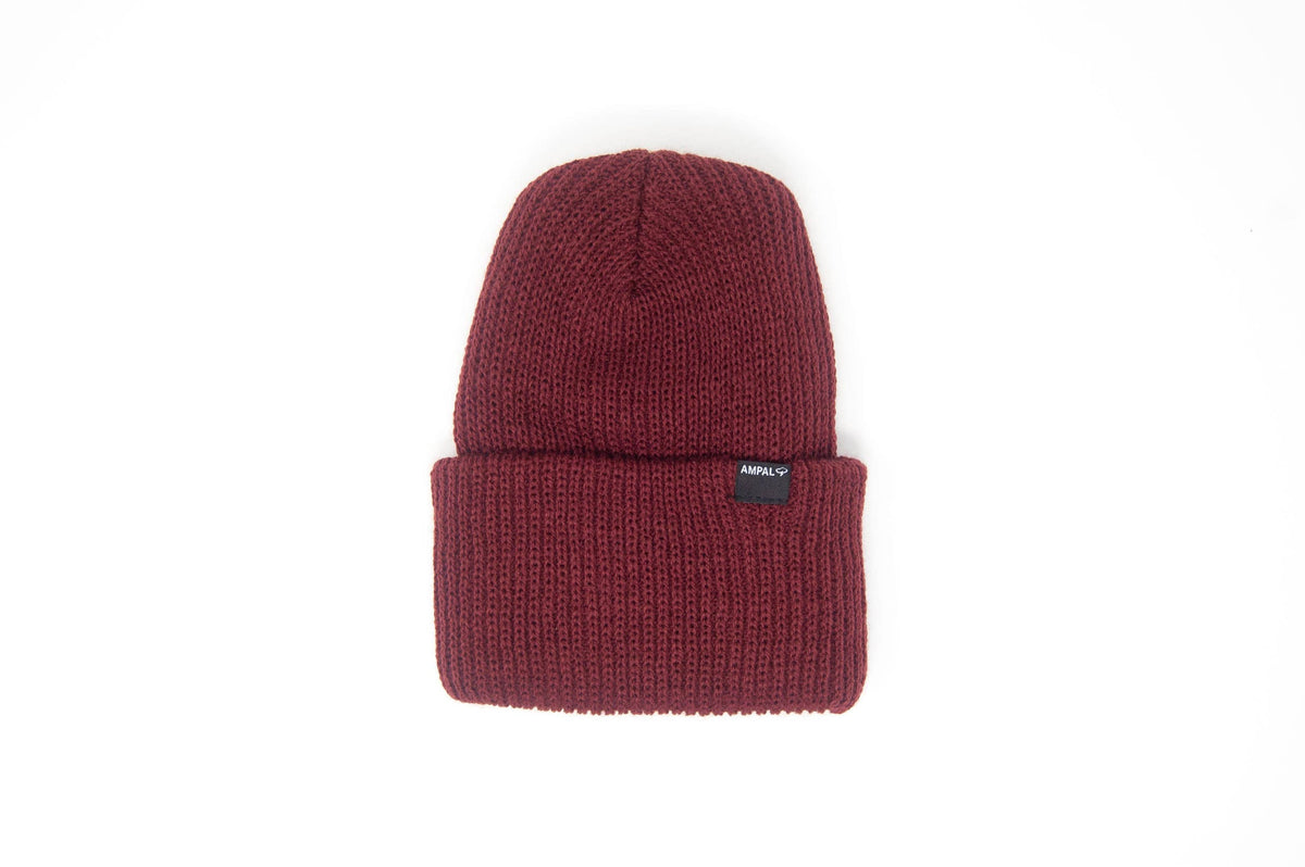 A dark burgundy ribbed knit beanie hat with a folded cuff and a small black brand tag on the side, shown against a plain white background.