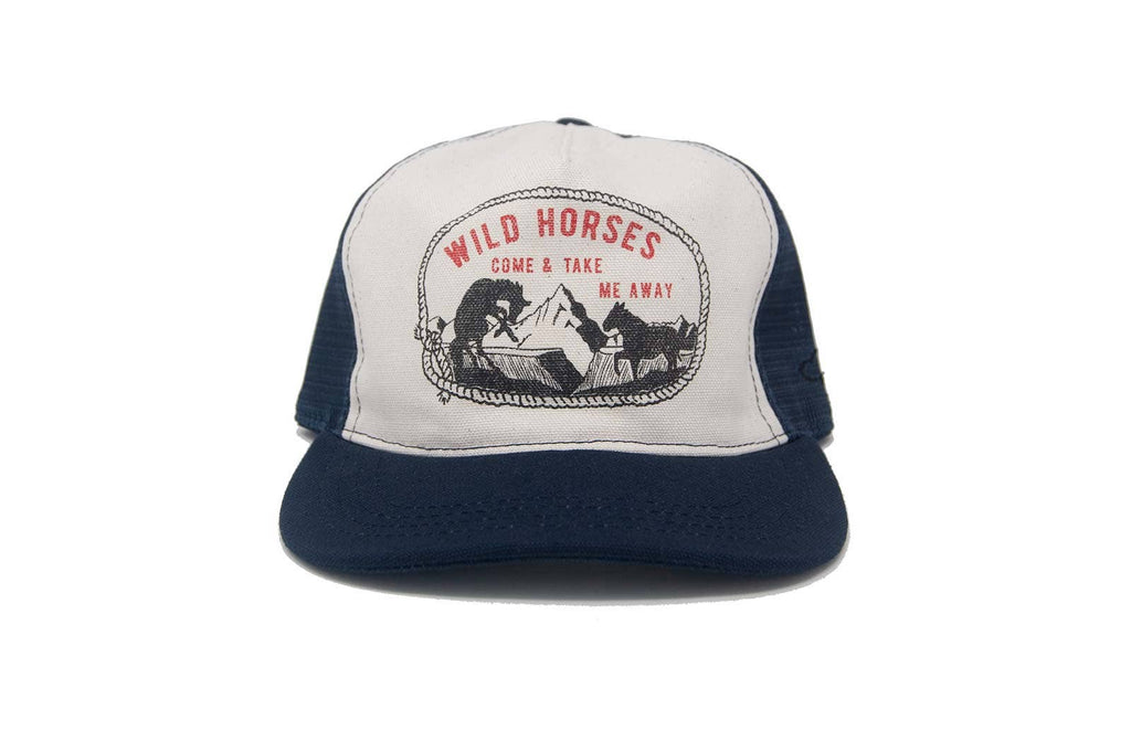 A trucker hat with a white front panel and navy blue brim and mesh back, featuring a circular graphic on the front that reads 'WILD HORSES COME & TAKE ME AWAY' with an illustration of horses and mountains.