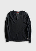 A black long-sleeve henley shirt with raglan sleeves, laid flat on a light gray background. The shirt features a three-button placket and a small brand patch near the bottom hem.