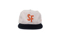 A structured baseball cap with an off-white crown, a dark navy flat brim, and a prominent orange embroidered 'SF' logo on the front, set against a plain white background.