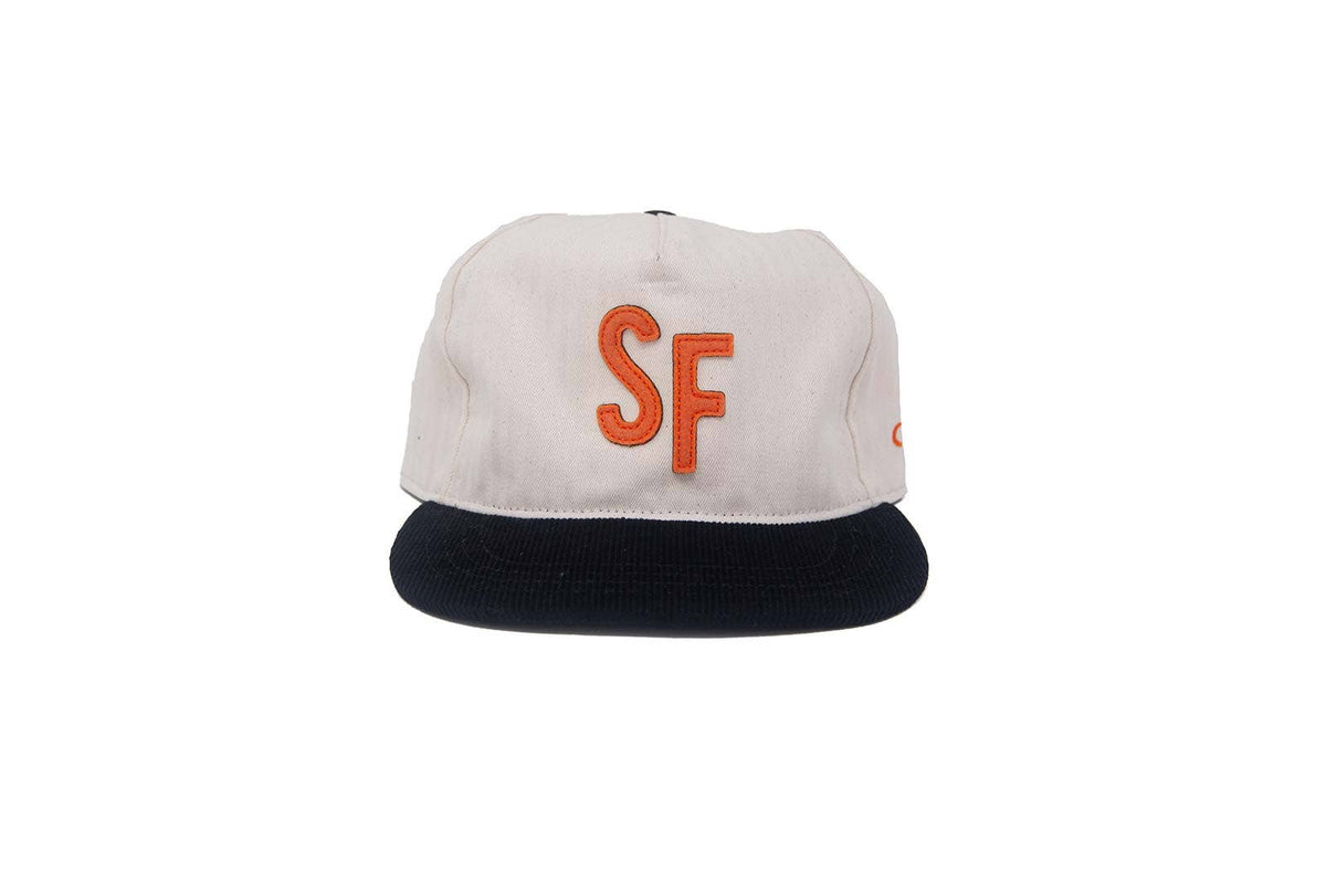 A structured baseball cap with an off-white crown, a dark navy flat brim, and a prominent orange embroidered 'SF' logo on the front, set against a plain white background.