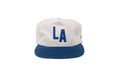 A white and blue LA snapback cap with a white crown, blue 'LA' lettering on the front, and a blue flat brim, shown against a plain white background.