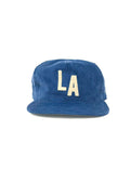 A blue corduroy 5-panel cap featuring the letters 'LA' embroidered in cream on the front, set against a plain white background.