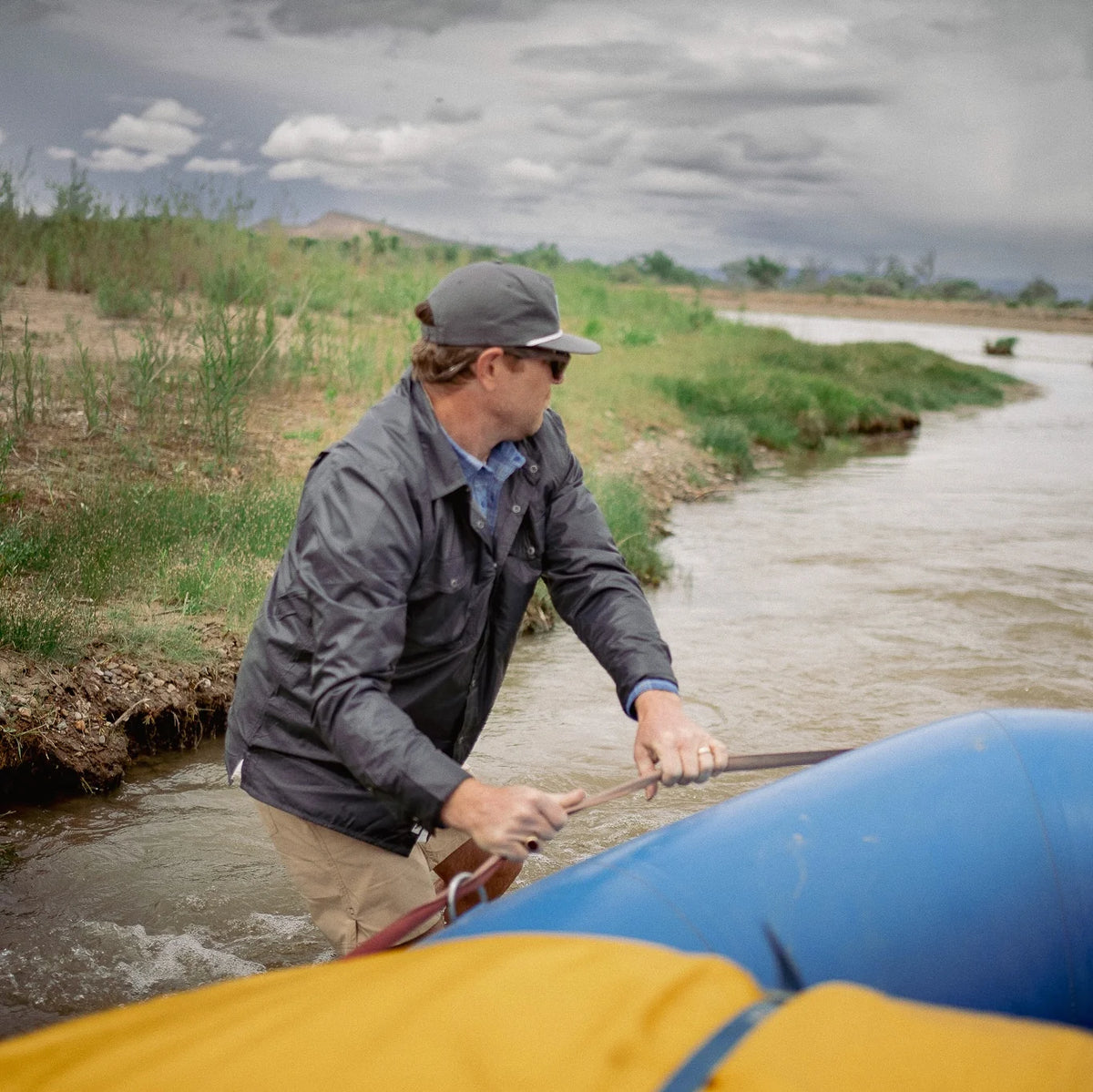 Man preparing to go rafting by a river with a cloudy sky.