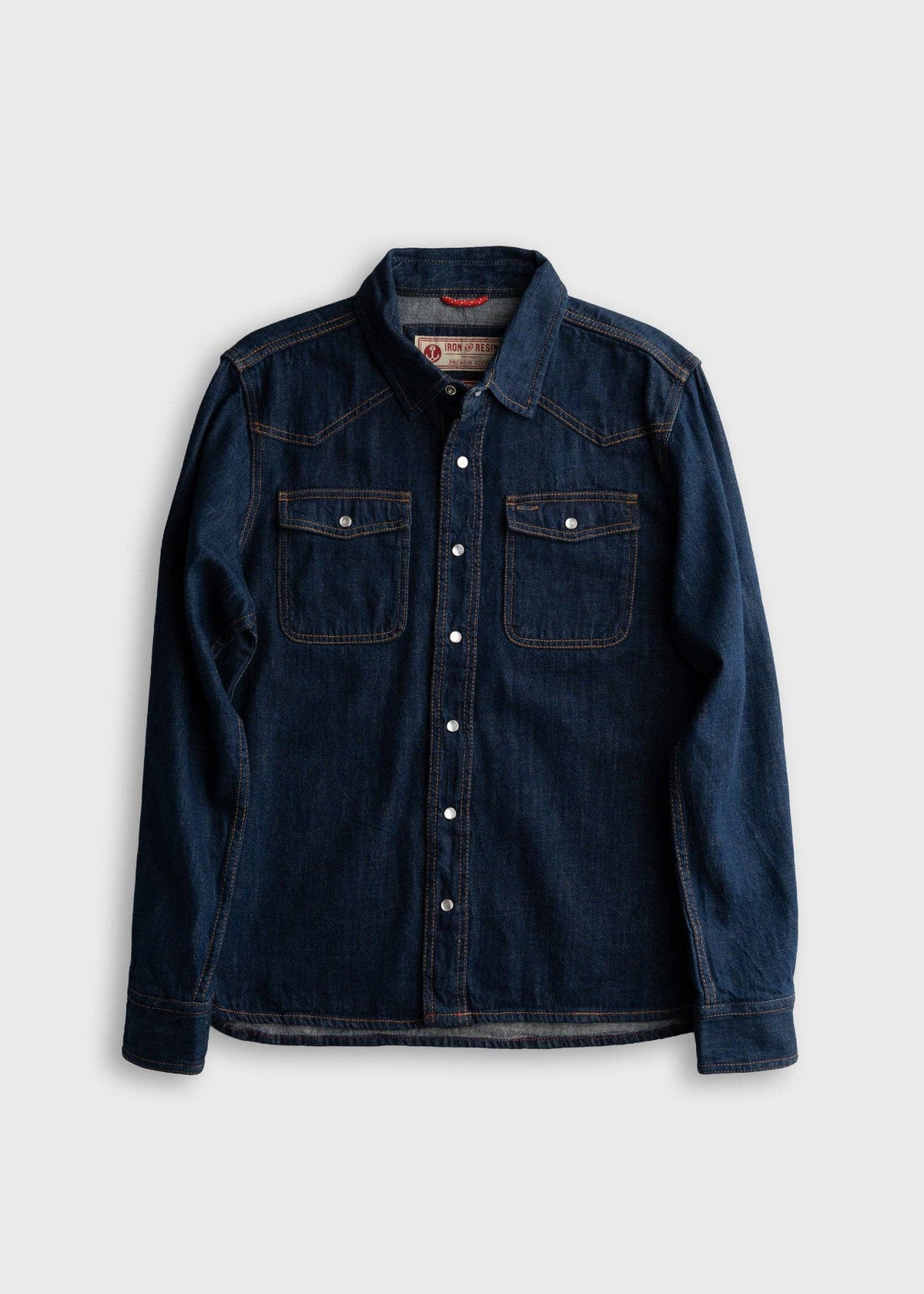 A dark blue denim long-sleeve button-up shirt with two chest pockets, laid flat against a light gray background.