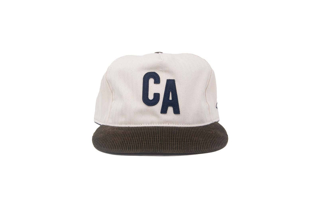 A structured baseball cap with an off-white crown featuring a dark navy blue 'CA' logo on the front, and a dark brown corduroy flat brim, shown against a plain white background.