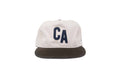 A structured baseball cap with an off-white crown featuring a dark navy blue 'CA' logo on the front, and a dark brown corduroy flat brim, shown against a plain white background.