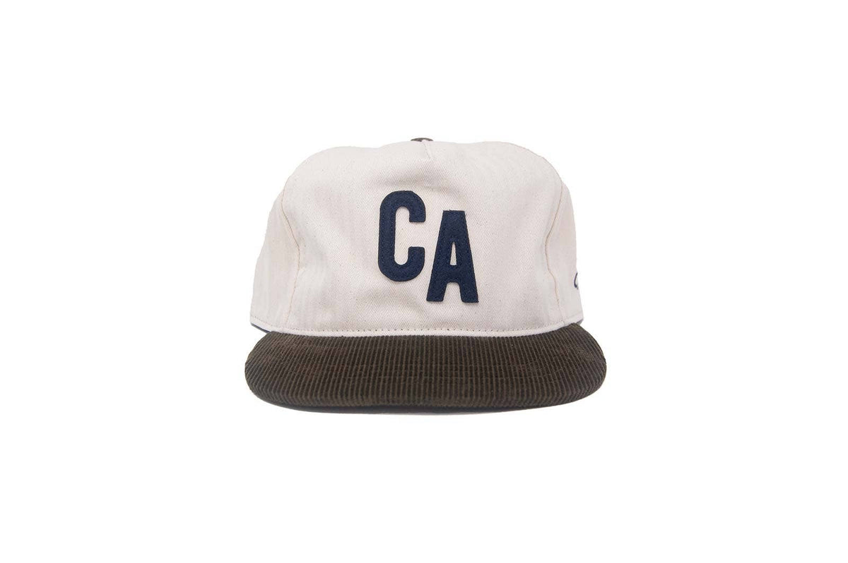 A structured baseball cap with an off-white crown featuring a dark navy blue 'CA' logo on the front, and a dark brown corduroy flat brim, shown against a plain white background.