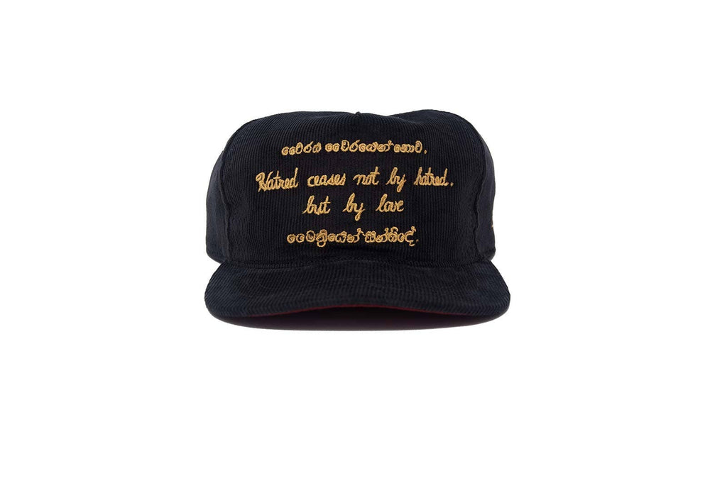 A black snapback cap with gold embroidered text "Hatred ceases not by hatred but by love" on the front panel, displayed against a solid white background.