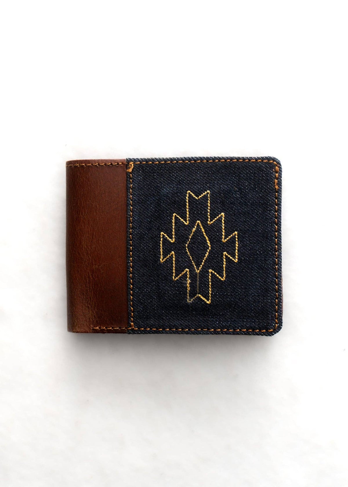 Denim wallet with brown leather patch and geometric design on a white background