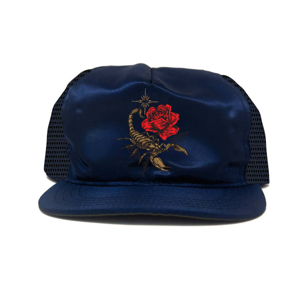 A navy blue satin trucker hat with black mesh back panels, featuring a red rose and gold scorpion graphic embroidered on the front panel.